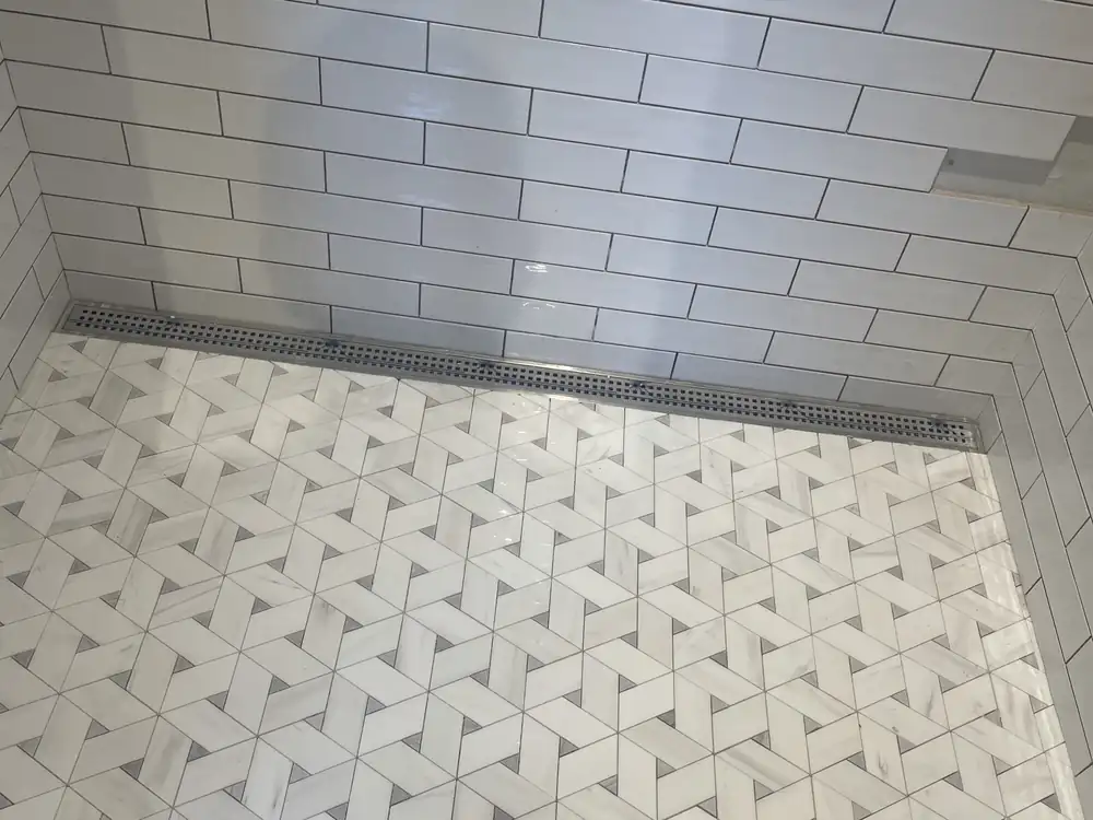 Marble mosaic shower floor with a stainless linear drain and subway tile walls