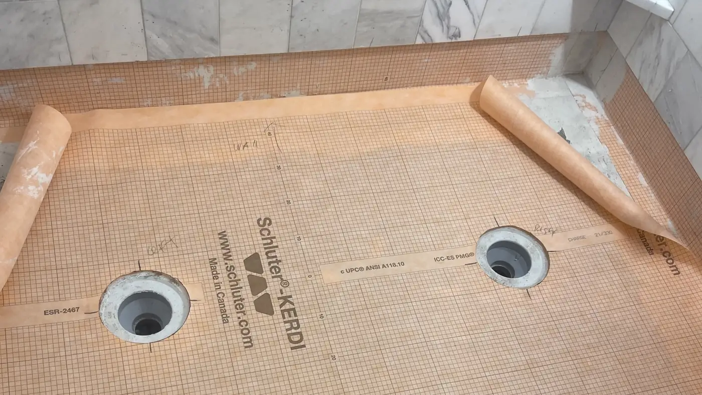 Schluter KERDI waterproofing membrane bonded over a shower pan with two drains